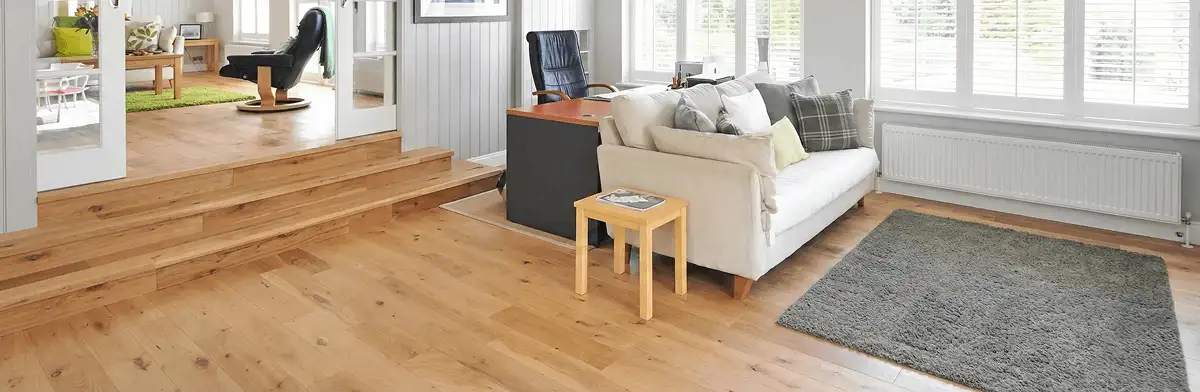 A modern living room with professionally installed laminate flooring, a beige sofa, a small side table, a gray rug, and large windows with white shutters in Denver, CO